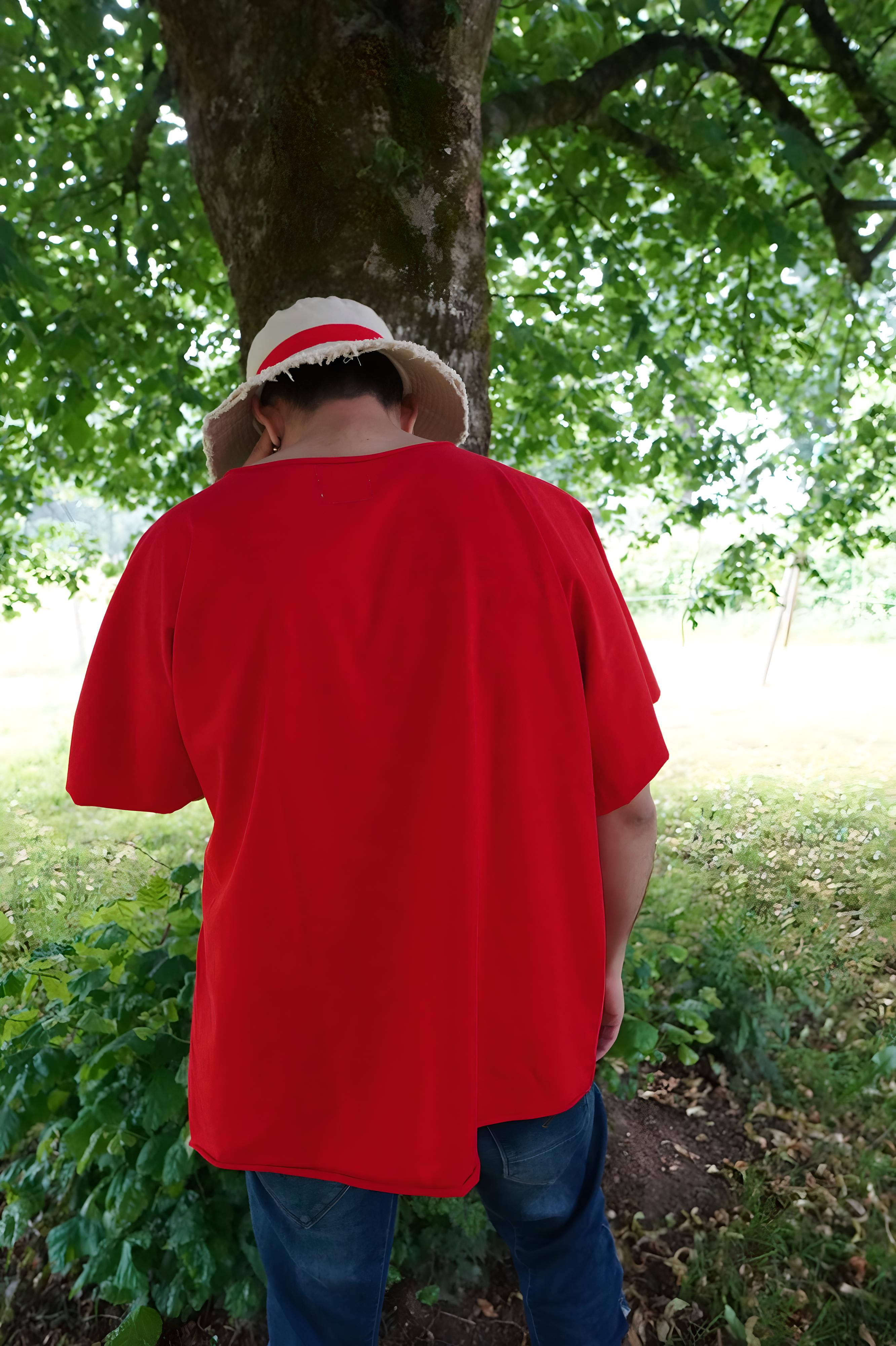 Vue arrière du t-shirt rouge oversize sans couture épaule, tombé fluide et brut, capté dans un environnement naturel sous un arbre.
