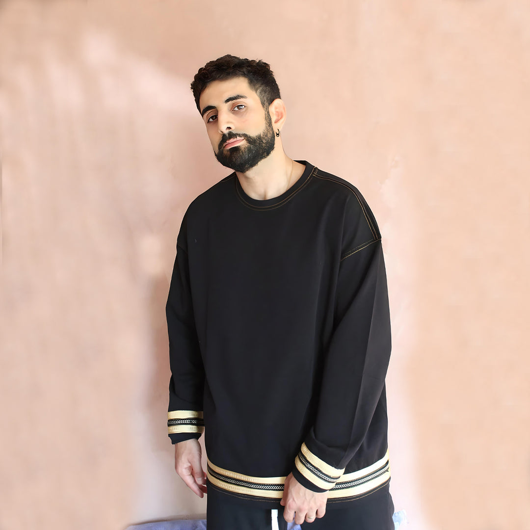 A front view of the Oversized Black and Gold Caftan Long Sleeve T-Shirt showcasing the exquisite gold embroidery and relaxed fit. The t-shirt's luxurious fabric is evident, reflecting the blend of contemporary streetwear and traditional Moroccan design.