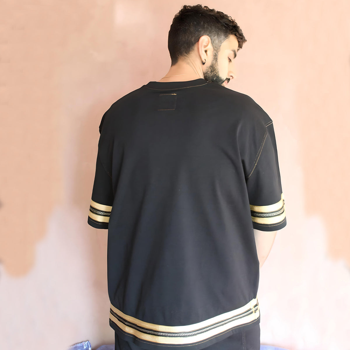 The model is showcasing the back view of the oversized black caftan t-shirt, adorned with elegant gold sfifa silk trims at the hem, highlighting the exquisite craftsmanship.