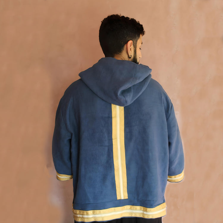 Rear view of the Oversized Linen Caftan Hoodie, showcasing the elegant golden Moroccan trim running down the center of the deep blue fabric.