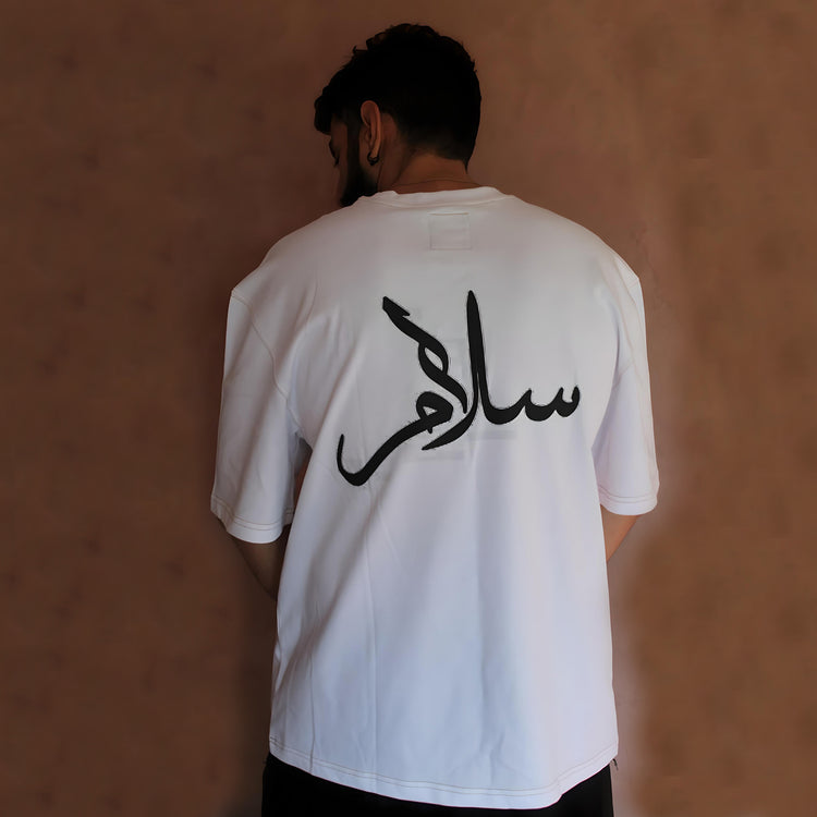 Back view of the Oversized White Jasmine Oasis T-Shirt featuring a stunning Arabic calligraphy design. The black Arabic script "السلام" (Peace) is prominently displayed, symbolizing serenity and sophistication. This minimalist design captures the essence of timeless elegance, making it perfect for those who appreciate urban streetwear with cultural significance. Crafted from premium cotton, this oversized tee offers unmatched comfort and style. Pair it with Kaizo-Ku joggers or shorts for a complete urban lo