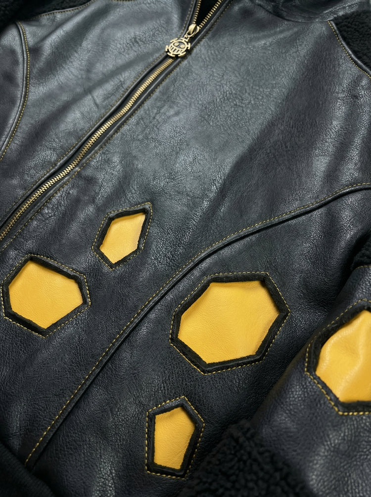 Gros plan sur les empiècements géométriques jaunes et le zip frontal d’une veste streetwear en similicuir noir. Finitions premium, inspiration univers pirate.