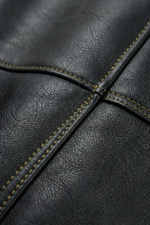 Gros plan sur le similicuir noir et les surpiqûres contrastées de la veste streetwear. Texture premium, finitions renforcées, style inspiré d’un univers pirate.