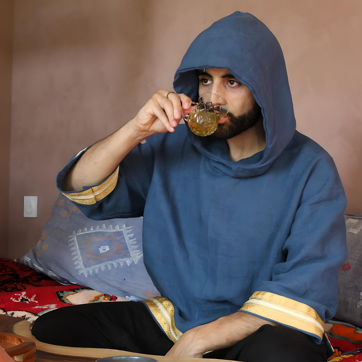 catch up of the model drinking a tea and wearin the hand made oversized caftan hoodie in blue.