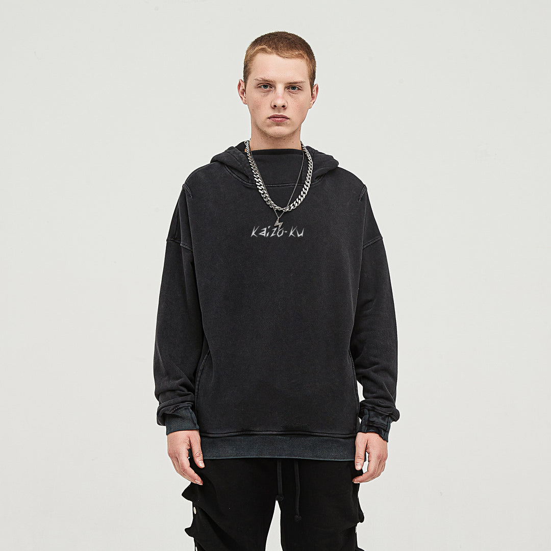 Male model wearing the oversized Kaizo-Ku hoodie in black. The embroidered logo stands out on the front, complemented by the turtle neck hood and thumb holes.