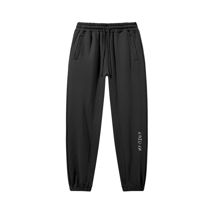 Flat front view of the Kaizo-Ku oversized jogger in Black. The embroidered logo on the left shin adds a subtle, stylish detail to this oversized piece.