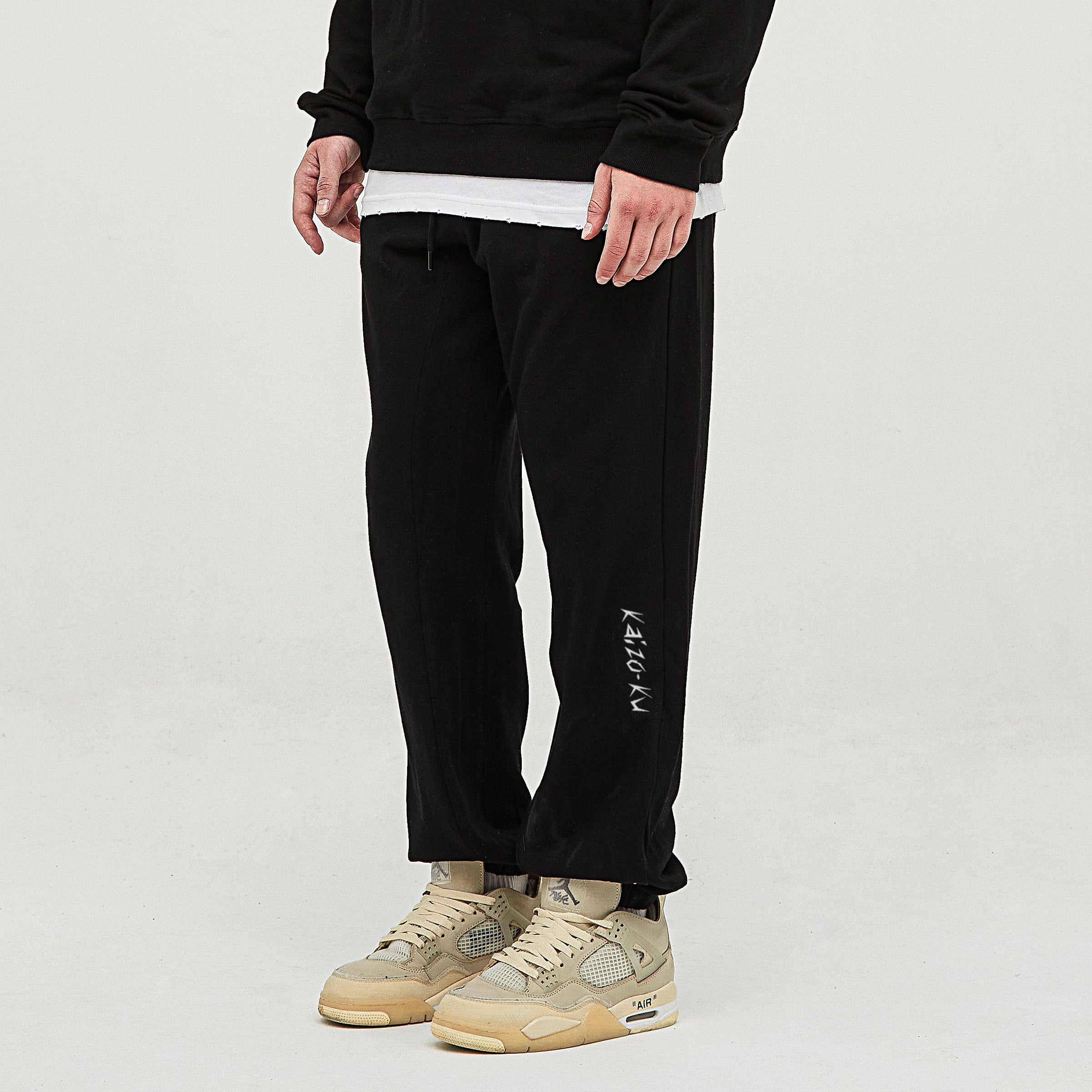 Left-side view of the Kaizo-Ku oversized jogger in Black, worn by the model. The embroidered "Kaizo-Ku" logo is clearly visible on the left shin, showcasing the brand’s signature streetwear aesthetic.