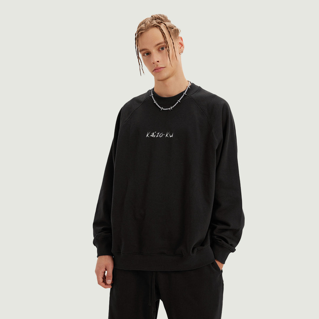 Male model wearing the Kaizo-Ku oversized sweatshirt in Black. Shows the relaxed, oversized fit and the embroidered "Kaizo-Ku" logo on the chest, perfect for a streetwear-inspired outfit.