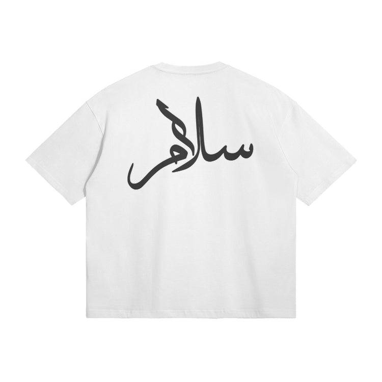 The back of the t-shirt features bold Arabic calligraphy spelling "سلام" (Peace) in black ink. The t-shirt is shown in white and is available in beige as well.