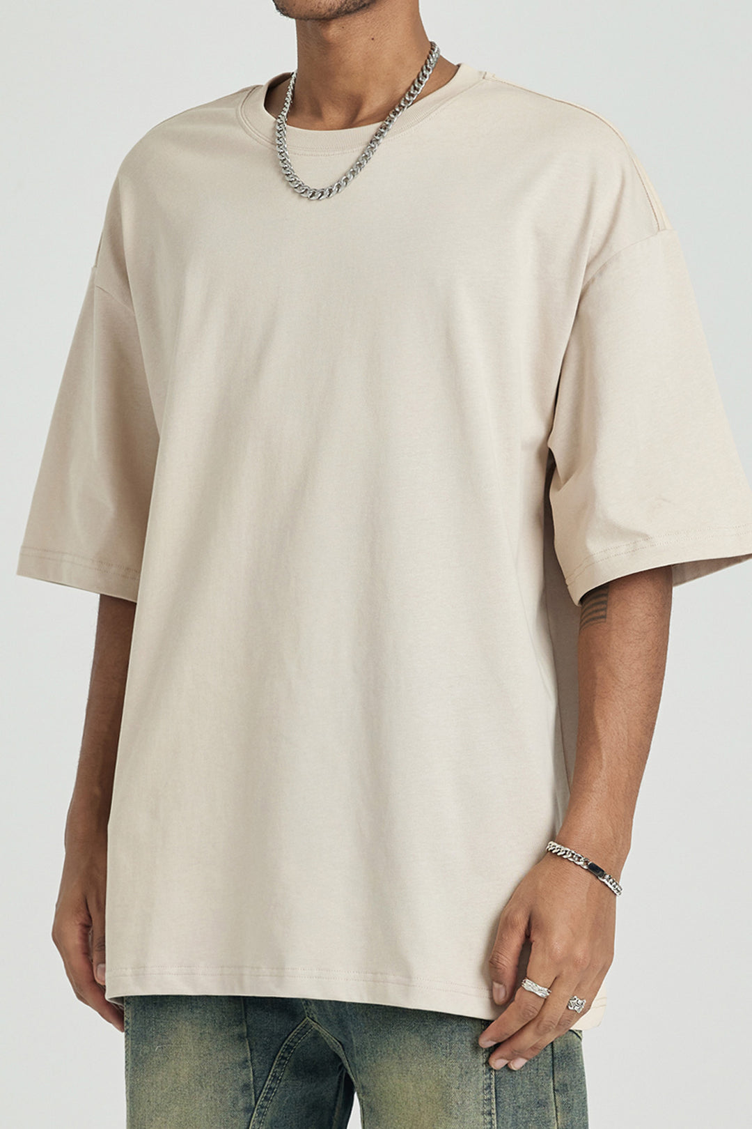 T-shirt oversize beige porté par un modèle, coupe drop shoulders, streetwear minimaliste.