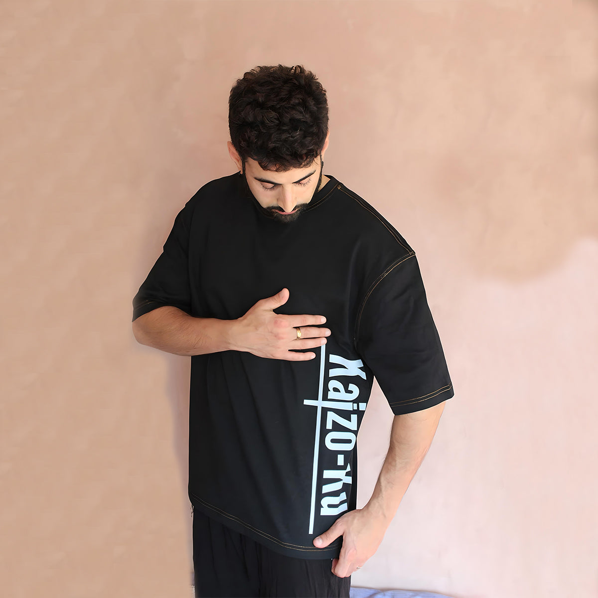 The model showcases the front of the oversized black t-shirt with the prominent Kaizo-Ku branding. The t-shirt's minimalist yet impactful design makes it versatile for any urban outfit.